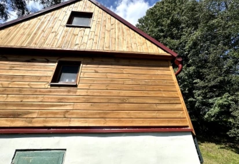 Štít rodinného domu s dřevěným obkladem, kde vedou rozvody klimatizace