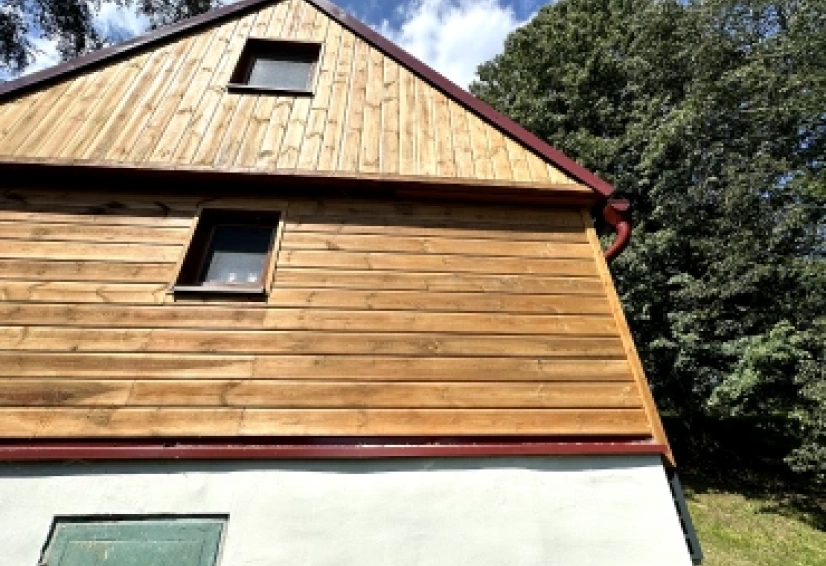 Štít rodinného domu s dřevěným obkladem, kde vedou rozvody klimatizace