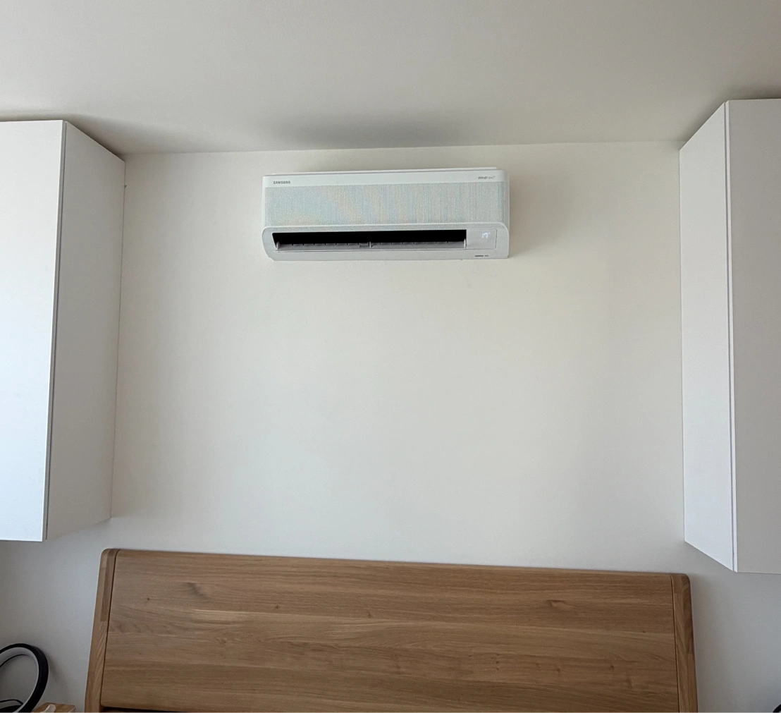 Nástěnná vnitřní klimatizační jednotka Samsung WindFree nad dřevěným čelem postele