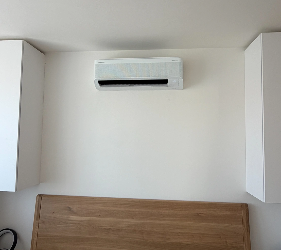 Bílá nástěnná vnitřní klimatizační jednotka Samsung WindFree nad čelem postele